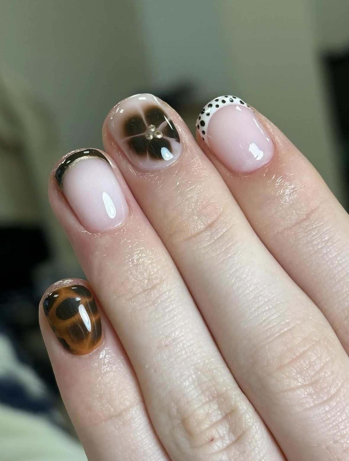 Korte nagels met nude basis en nail art: schildpadmotief, bloem met goudsteentjes en een French met stippen